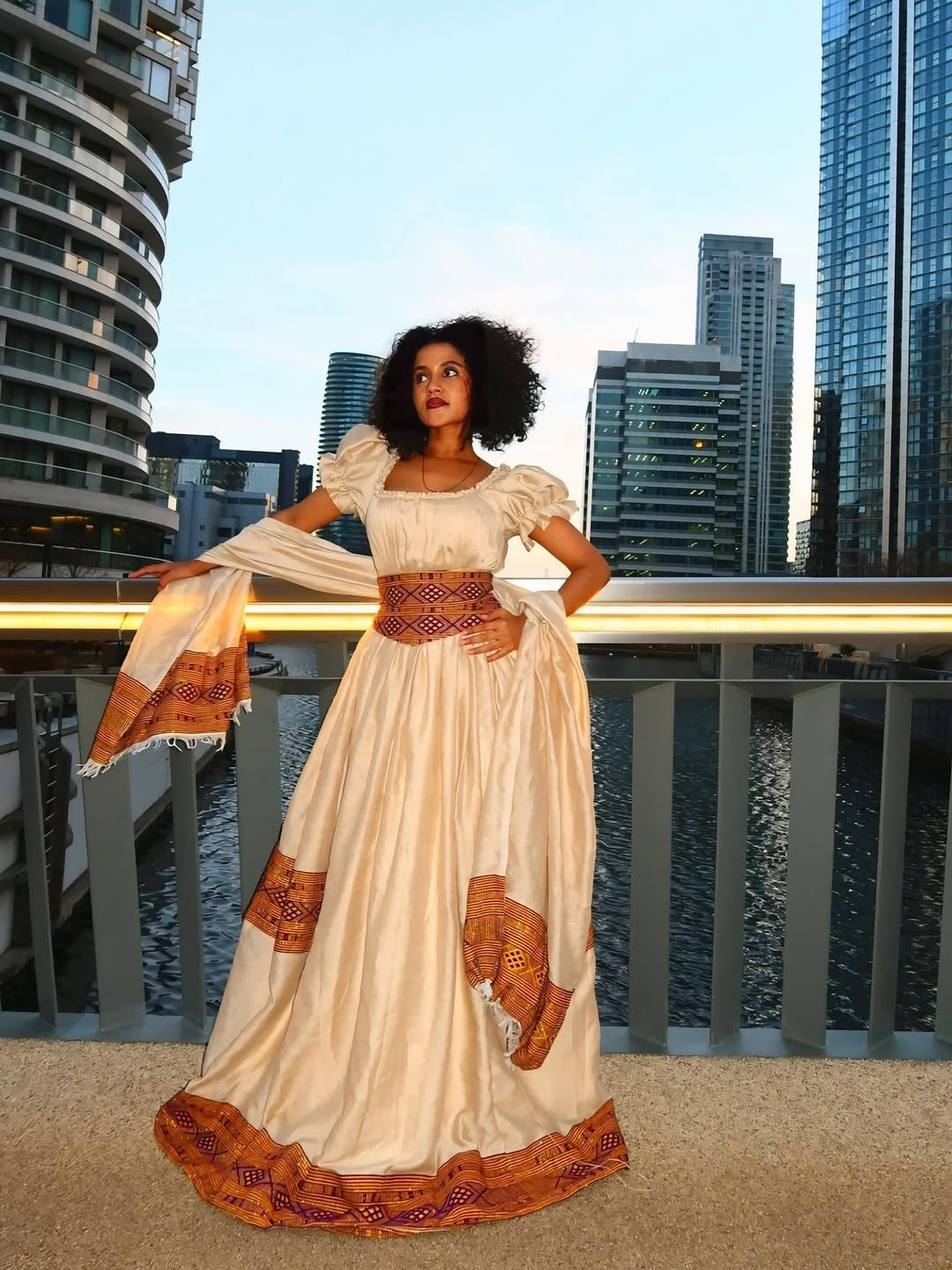 Woman in a longBrown Habesha Libs standing on a rooftop with city skyline in the background