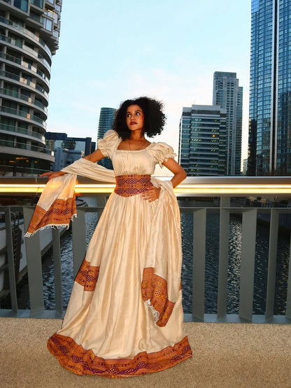 Woman in a longBrown Habesha Libs standing on a rooftop with city skyline in the background