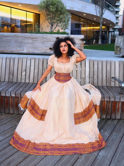 Woman in a traditional Brown Habesha Libs standing outdoors with modern building in the background