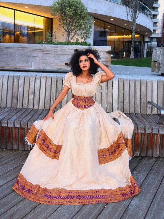 Woman in a traditional Brown Habesha Libs standing outdoors with modern building in the background