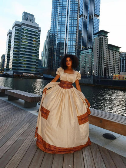 Woman in a Brown Habesha Libs standing on a dock with city skyline in the background