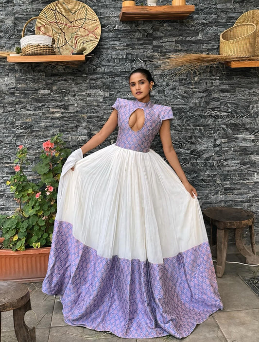 Woman in a two-tone  Habesha dress sitting against a stone wall with plants.