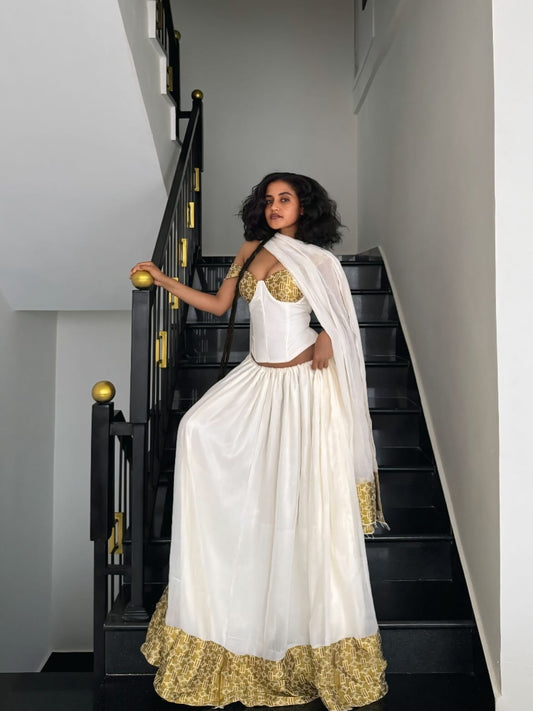 Woman in a white and gold traditional Habesha dress standing on a staircase.