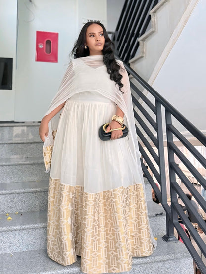 A woman stands on outdoor concrete stairs wearing a traditional ethiopian dress consisting of a white and beige patterned dress with a sheer white dupatta. She is holding a small black clutch bag with gold detailing.