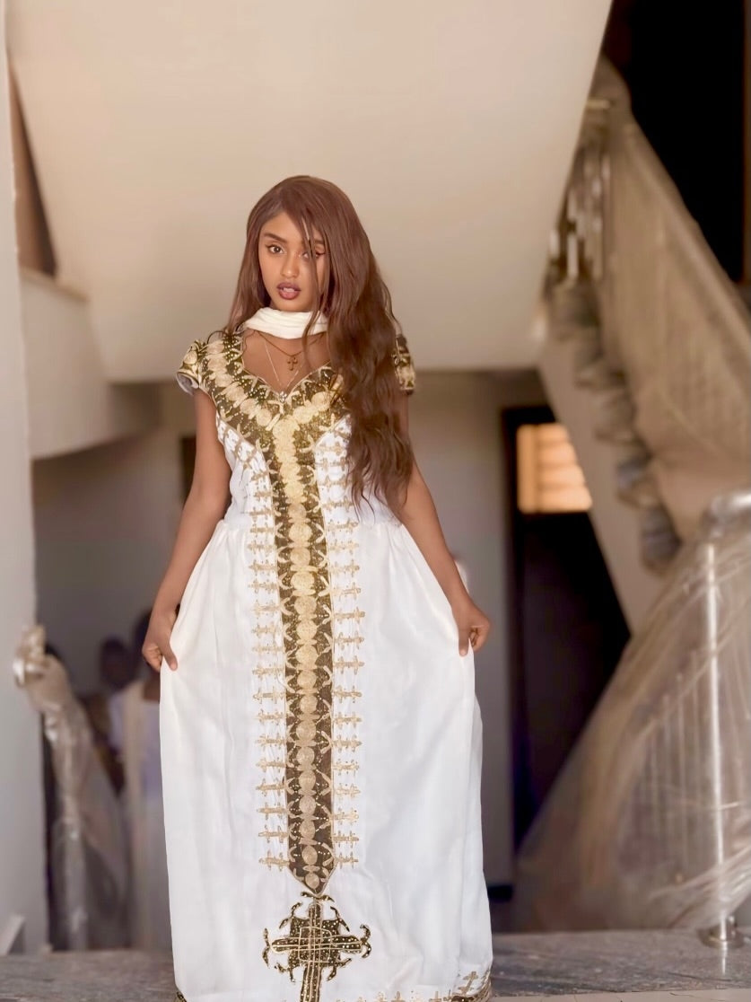 Woman wearing a white Habesha Dress with gold embroidery in an indoor setting