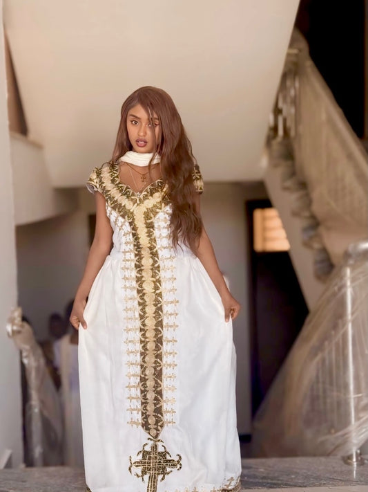 Woman wearing a white Habesha Dress with gold embroidery in an indoor setting
