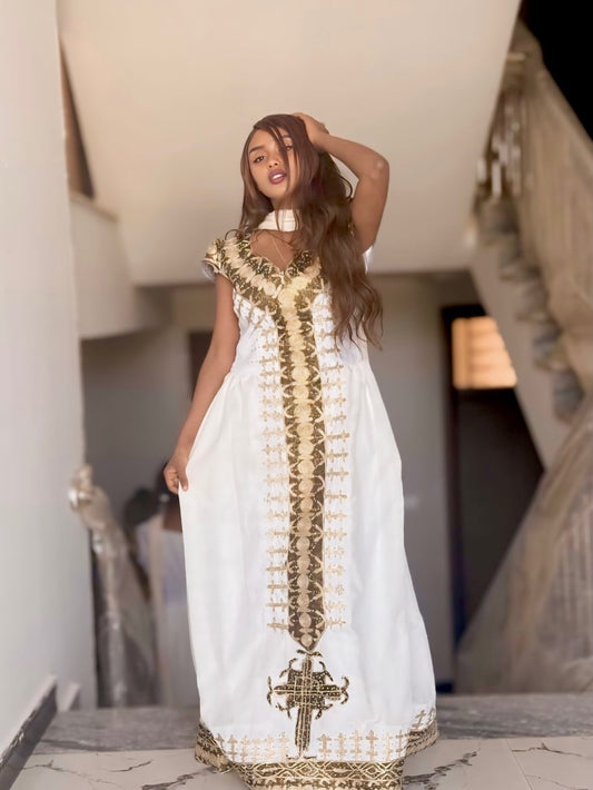 Woman wearing a white Habesha Dress with gold embroidery in an indoor setting