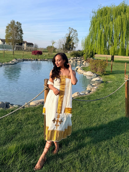 Woman in a patterned Ethiopian National Dress standing by a pond with greenery in the background