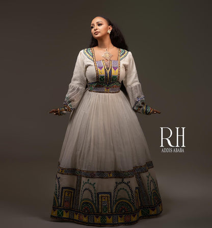 A woman modeling a traditional long white Axum fetil  with colorful embroidered details and a patterned hem, posed against a dark gray studio background. The brand text 'RH ADDIS ABABA' is visible on the right.