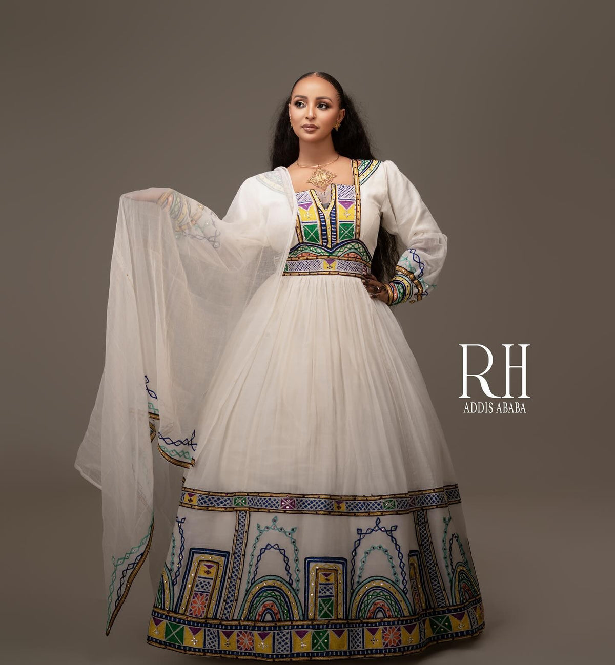 A woman models a traditional Ethiopian white Axum fetil with colorful embroidered patterns and a matching sheer white dupatta, set against a solid gray studio background. The brand logo 'RH ADDIS ABABA' is visible on the right.