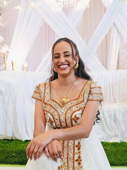 Woman in a decorated outdoor setting wearing a gold and white habesha kemis.
