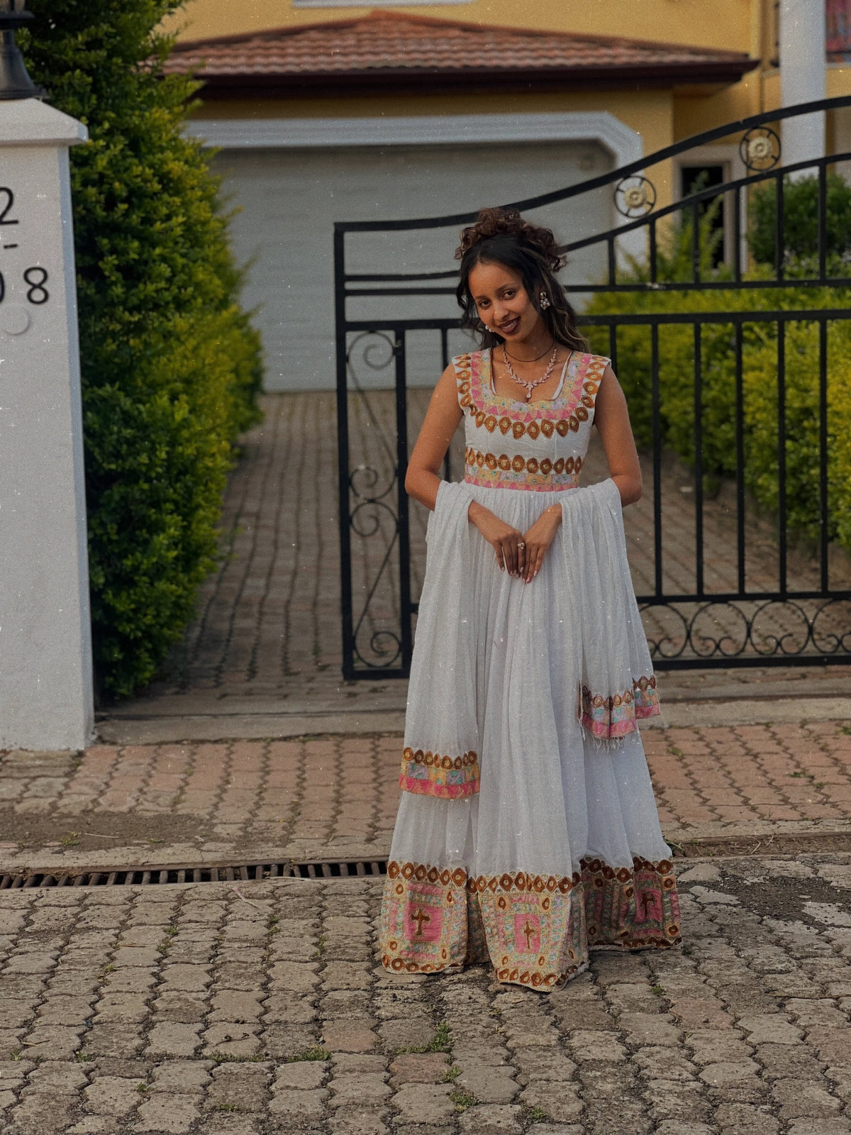 Woman in traditional Ethiopian Dress standing on a paved path with a house in the background