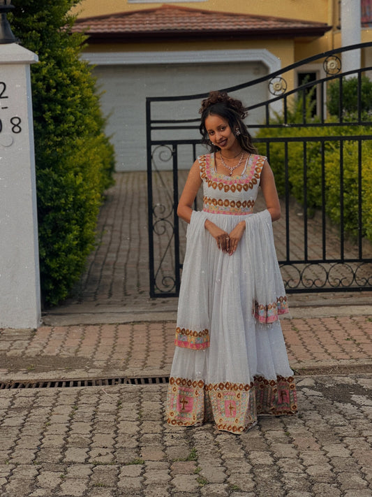 Woman in traditional Ethiopian Dress standing on a paved path with a house in the background