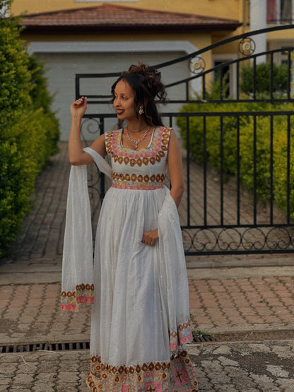 Woman in a traditional Ethiopian Dress standing outdoors with a house and gate in the background