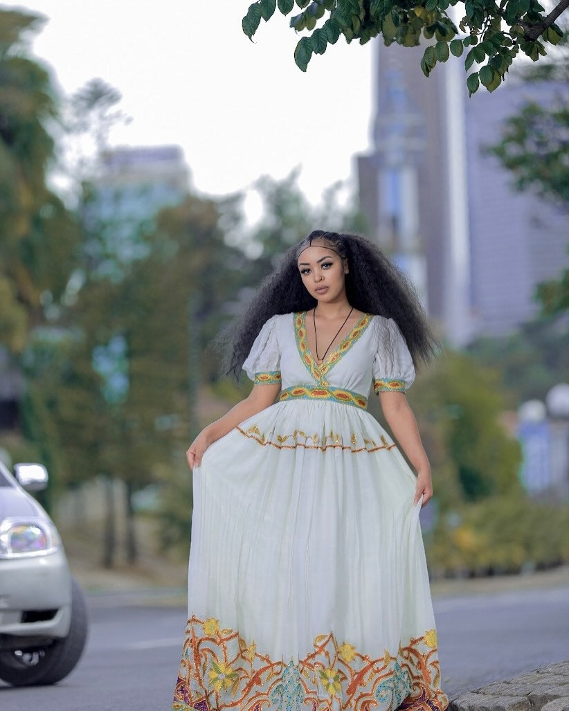 Woman in a long, white dress with colorful patterns standing outdoors.