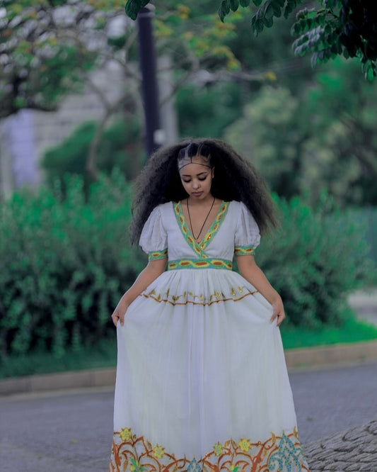 Woman in a white dress with colorful embroidery standing outdoors.