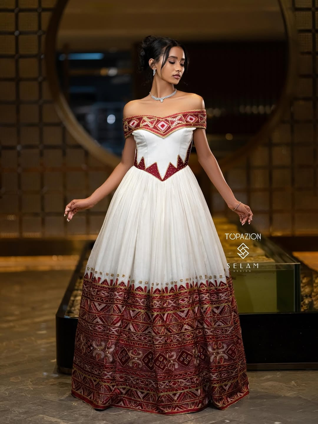 Woman wearing a white and red patterned Ethiopian dress  in an indoor setting