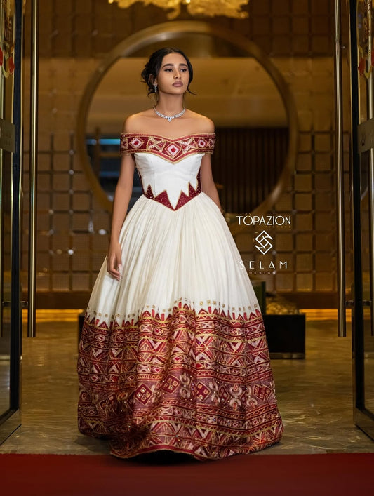 Woman in a white and red patterned Ethiopian dress standing in front of a mirror with 'Topazion' branding.