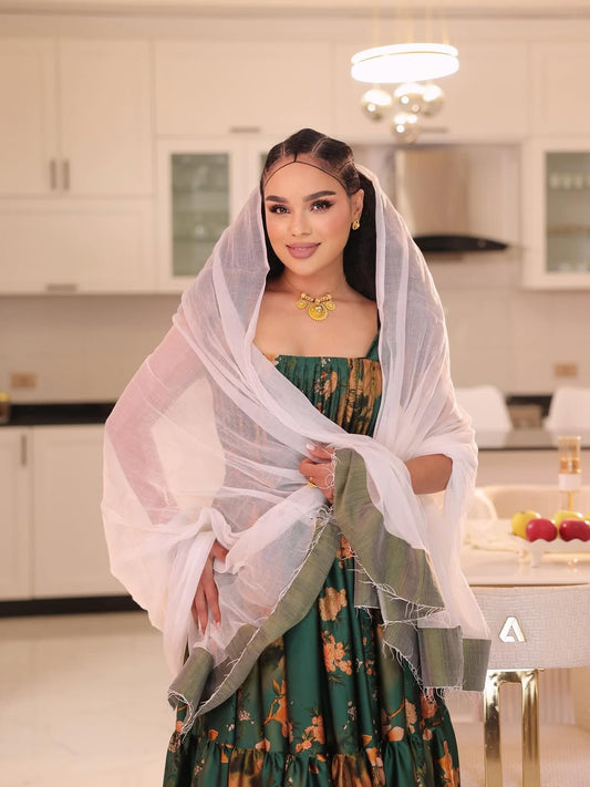 Woman in a green traditional habesha shiffion with a white dupatta in a kitchen setting