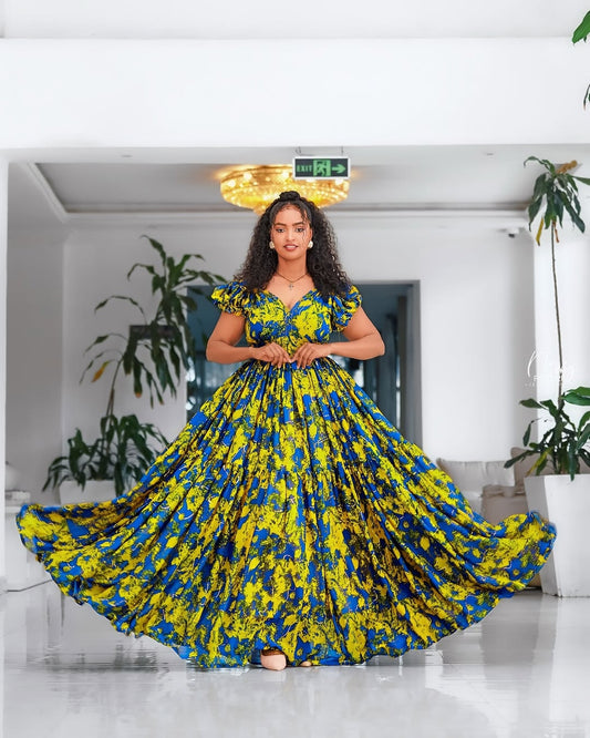 Woman in a blue and yellow floral Yellow and Green Shiffon Ethiopian Dress standing in a modern indoor setting.