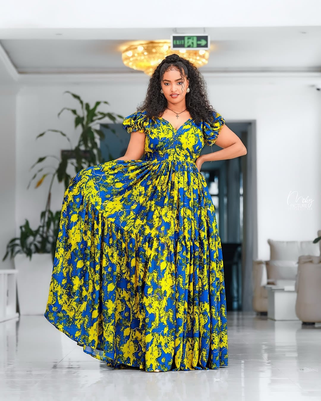 Woman wearing a blue and yellow floral Yellow and Green Shiffon Ethiopian Dress in an indoor setting