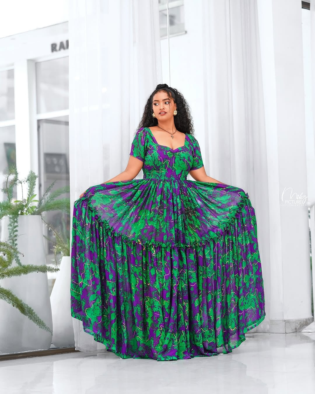 Woman wearing a green and purple Green Habesha Shifion  in a bright room.