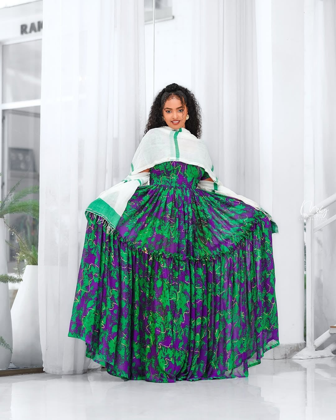 Woman wearing a green and purple Green Habesha Shifion  in a bright room.