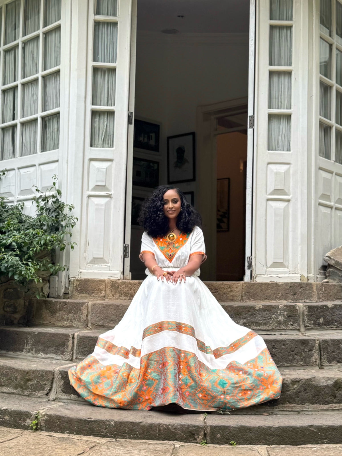 Woman in a colorful Ethiopian Dress sitting on steps outside a building