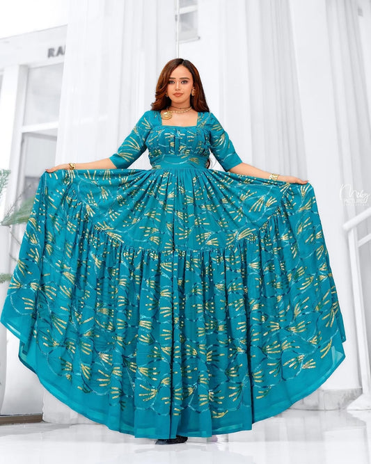 Woman holding up a teal chiffion dress with gold patterns in a bright room.