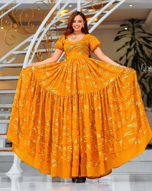 Woman wearing a yellow dress with a floral pattern in an indoor setting.