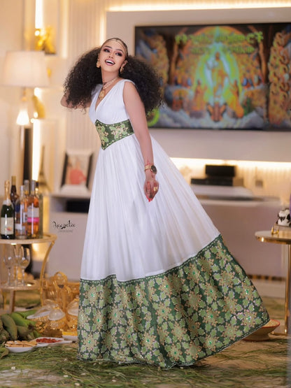 Woman in a white and green Ethiopian dress standing in a decorated room with a colorful painting on the wall.