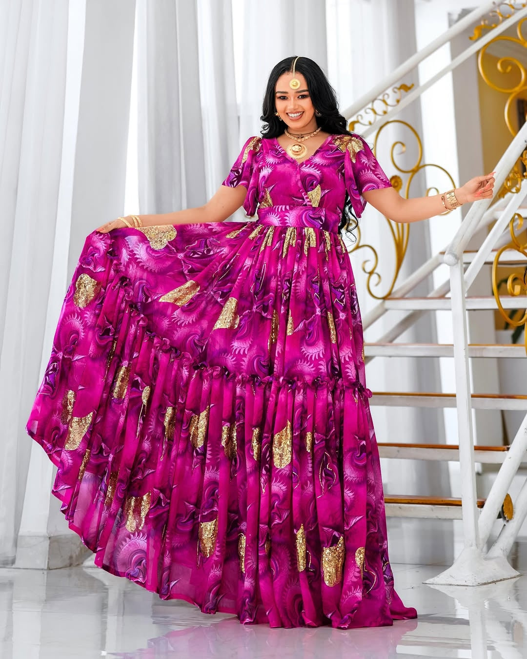 Woman in a vibrant pink and gold traditional habesha chiffion standing on a staircase.
