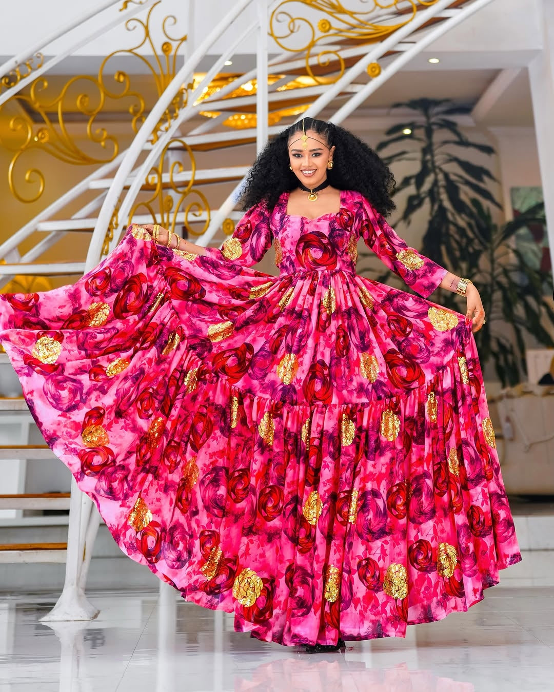 Woman in a vibrant pink Habesha chiffion  with gold patterns standing in a decorated interior setting.