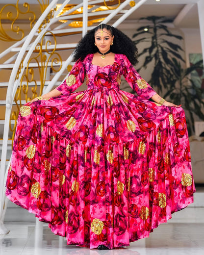 Woman in a vibrant pink Habesha Chiffon with red floral patterns standing in a decorated interior setting.