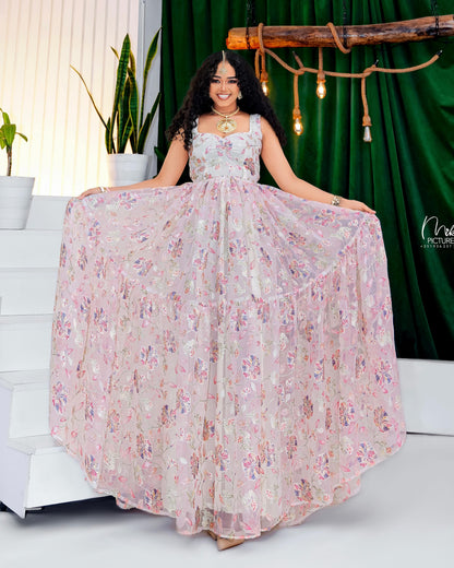 Woman in a floral Habesha Kemis posing in front of a green curtain with decorative lights.