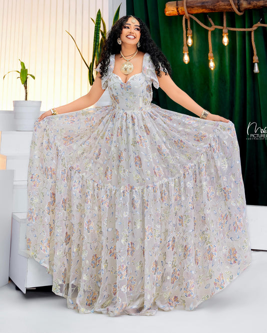 A woman modeling a voluminous, tiered A-line ball chiffon Habesha with a floral print. The dress features a sweetheart neckline, short puff sleeves, and a fitted bodice.