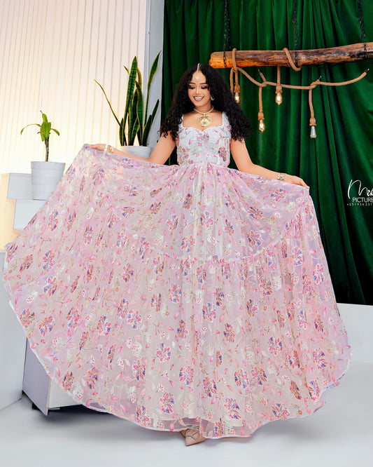 Woman in a floral Habesha Kemis holding it out in a room with green curtains and plants.