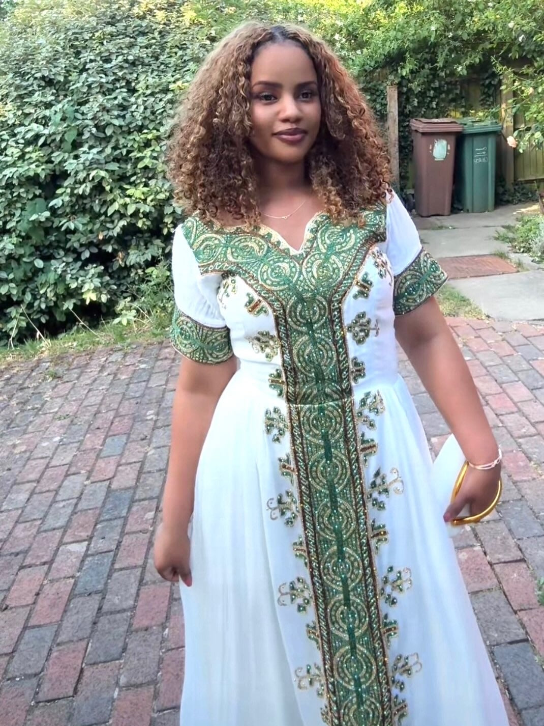 Woman wearing a white and green traditional habesha Dress standing outdoors.