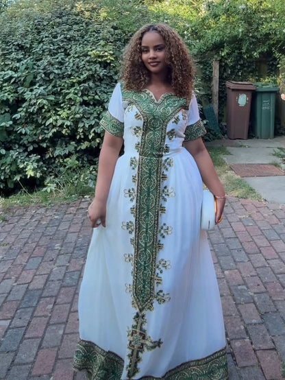 Woman wearing a white habesha Dress with green embroidery standing outdoors.