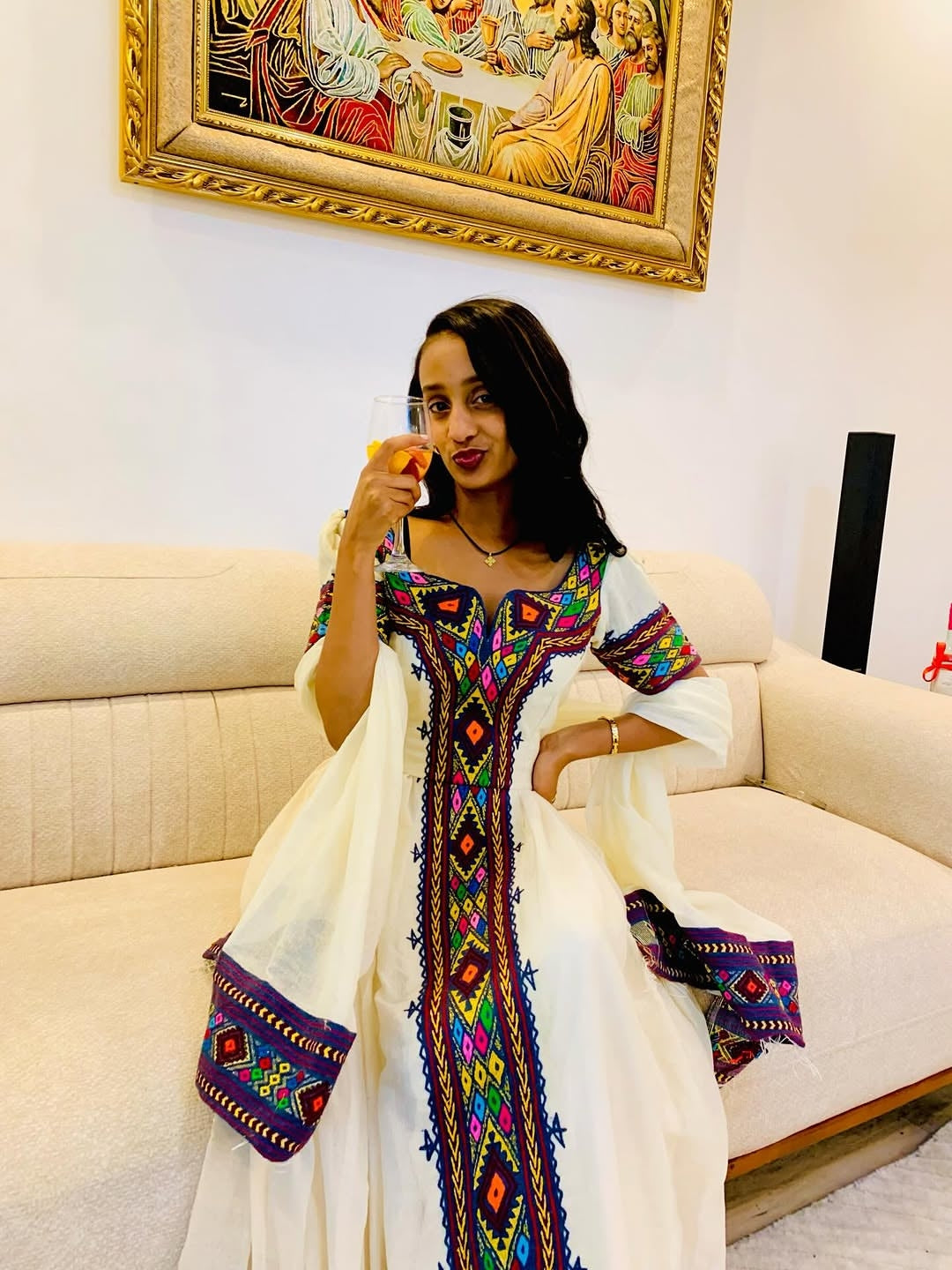 Woman in a colorful embroidered have dress sitting on a couch with a painting in the background