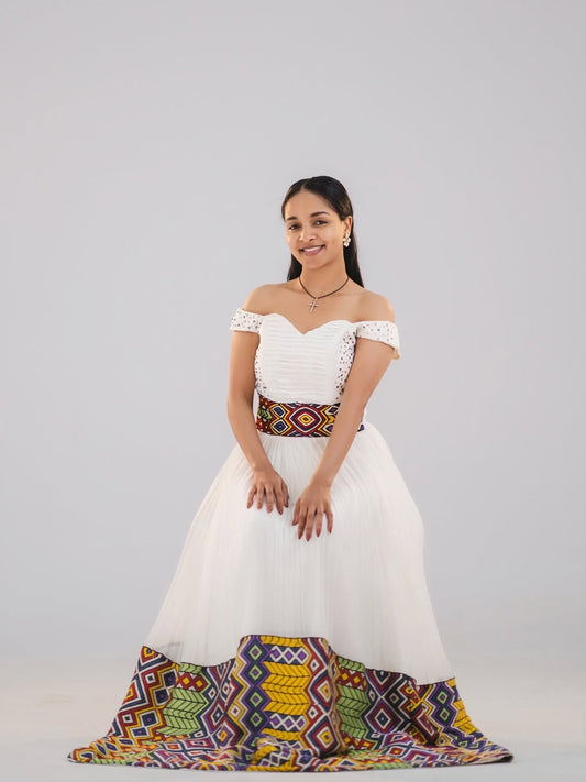 Woman in a white and green habesha dress in an elegant interior setting.