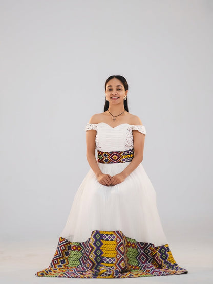 Woman in a white and gold habesha dress in an elegant interior setting.