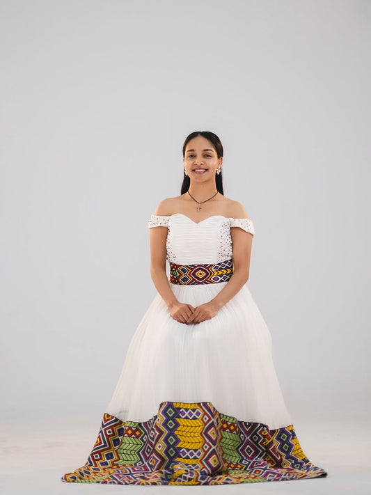 Woman in a white and gold habesha dress in an elegant interior setting.