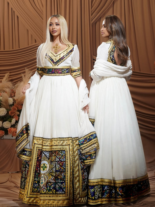 Two women modeling traditional white Habesha Dress with ornate gold, blue, and red embroidered borders, posed against a draped brown backdrop.