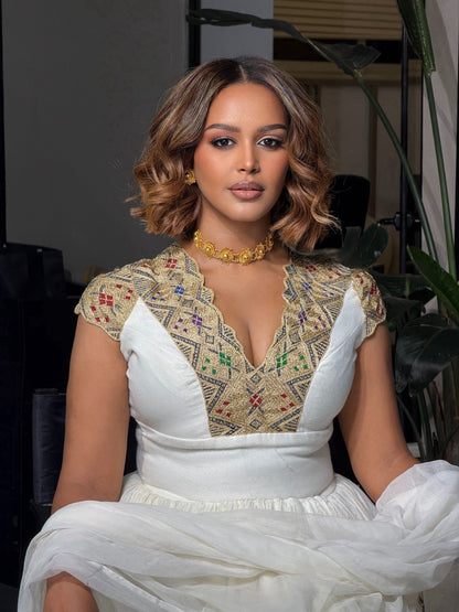 Woman wearing a white Habesha Kemis with a patterned top in an indoor setting