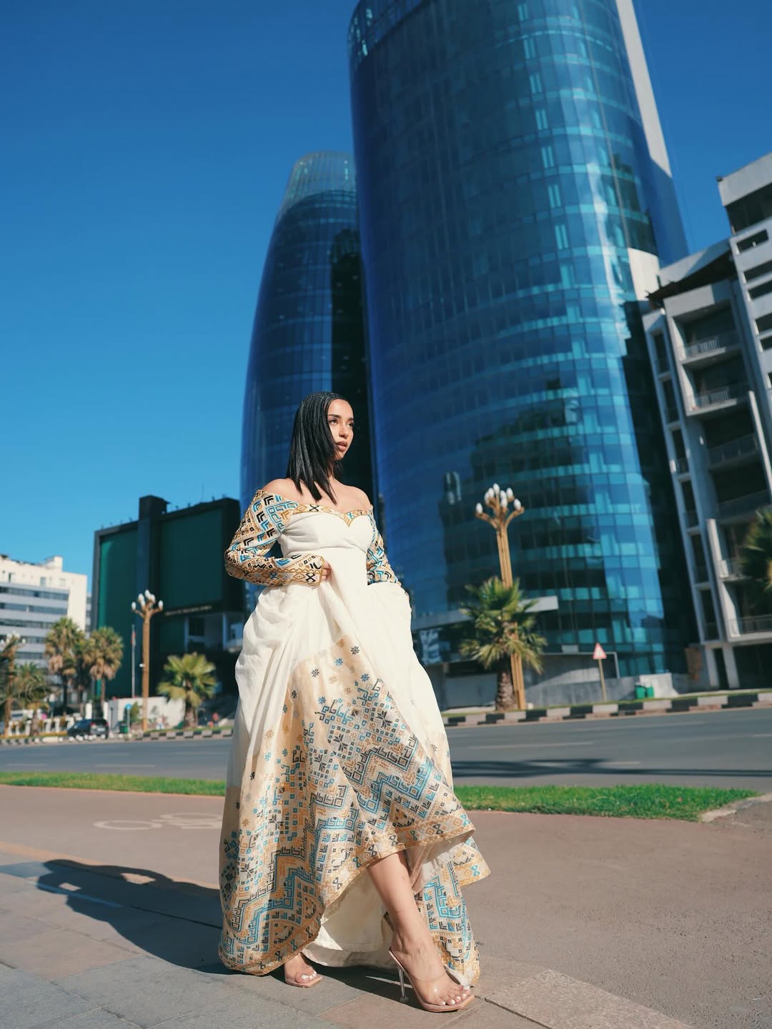 Woman in a long, patterned Ethiopian dress standing in front of modern buildings.