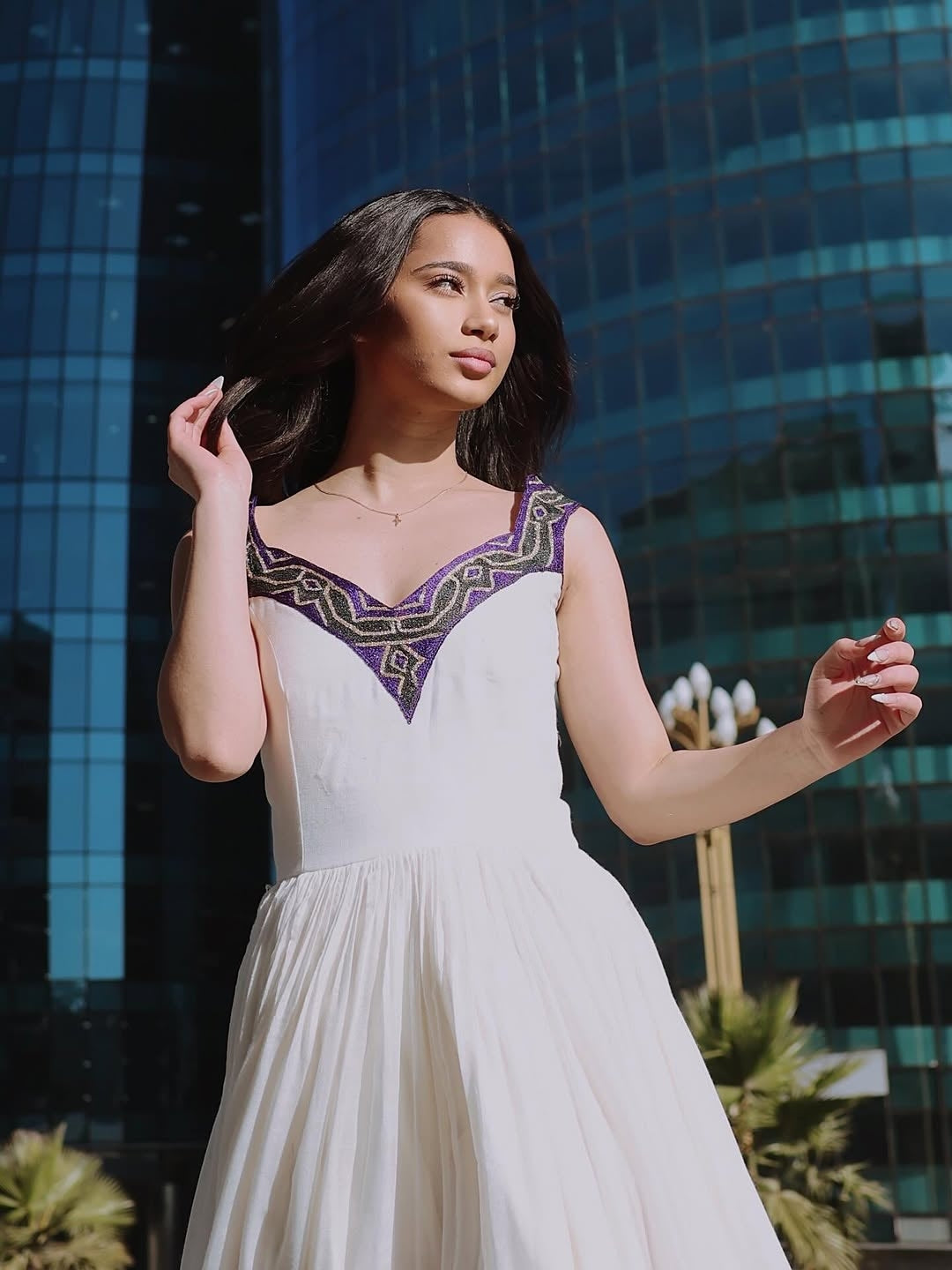 Woman in a white Ethiopian dress with purple accents standing in front of a modern building.