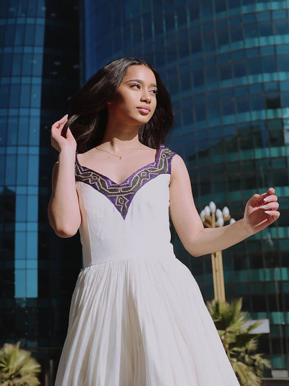 Woman in a white Ethiopian dress with purple accents standing in front of a modern building.