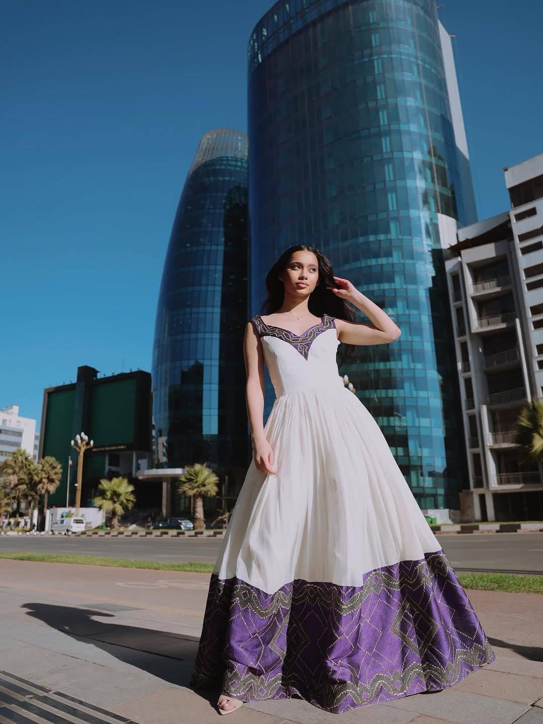 Woman in a white and purple Ethiopian dress  standing in front of modern buildings