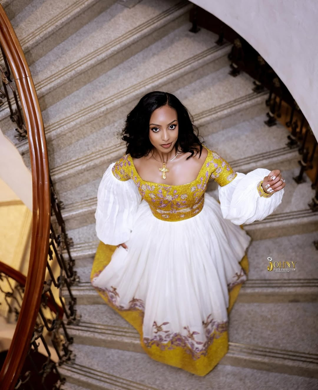 Woman in a yellow and white Gold Ethiopian Kemis standing on a staircase